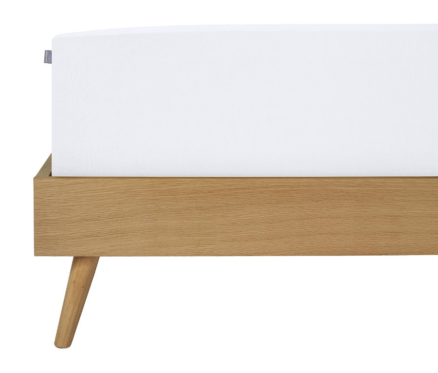 Detailansicht eines Bettes mit einem weißen Laken und einem Holzrahmen.