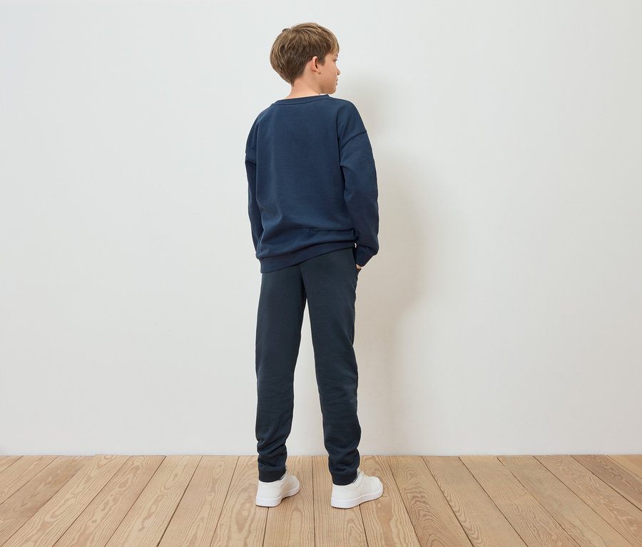 Ein Junge in einem blauen Sweatshirt und blauen Hosen steht mit dem Rücken zur Kamera.