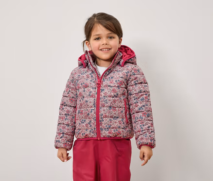 Ein Mädchen trägt eine geblümte Jacke und eine pinke Hose.