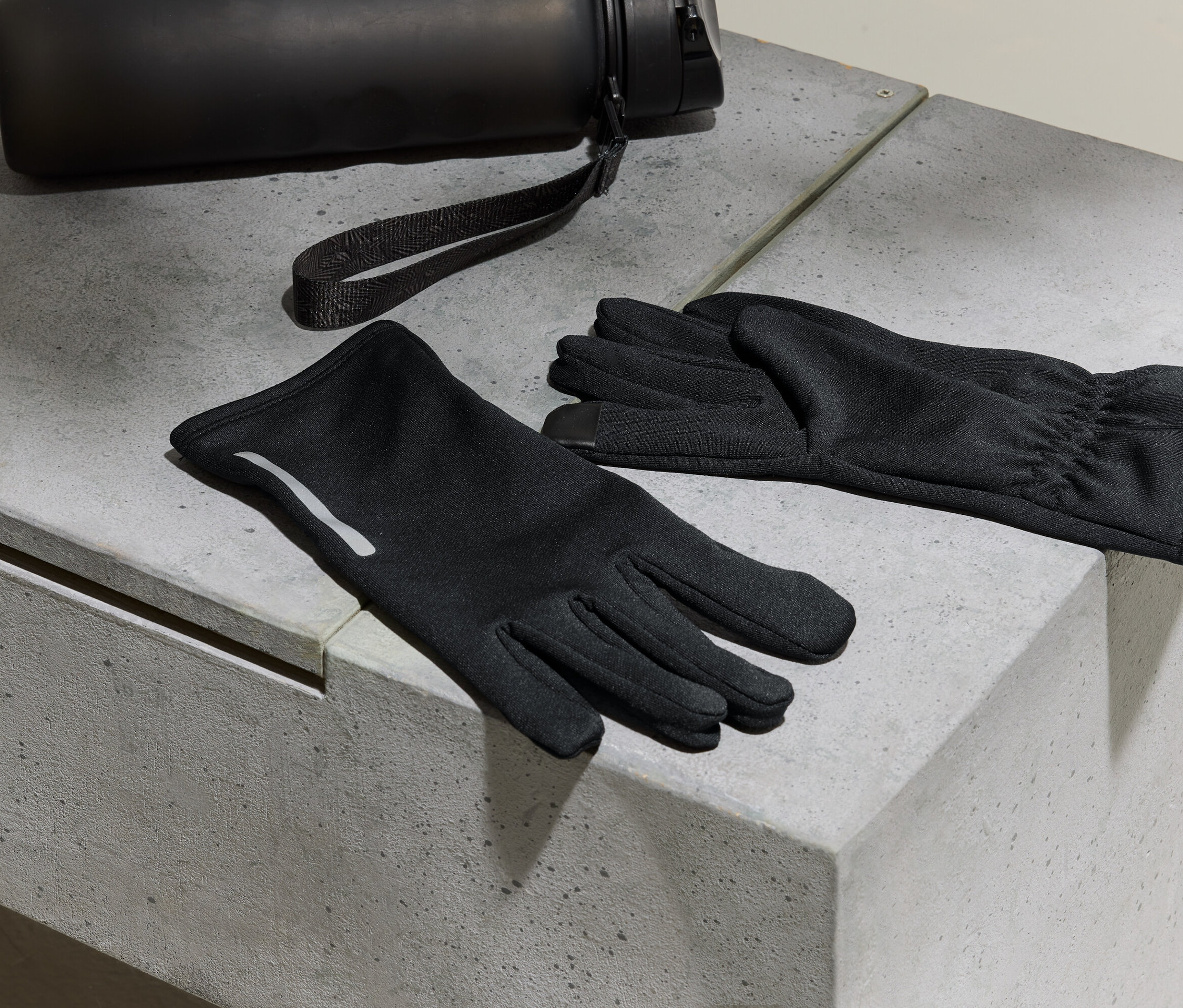 Schwarze Handschuhe und eine Wasserflasche liegen auf einer Betonoberfläche.