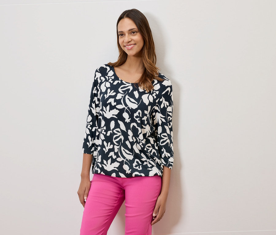Frau trägt eine dunkelblaue, blumengemusterte Bluse und pinke Hosen.