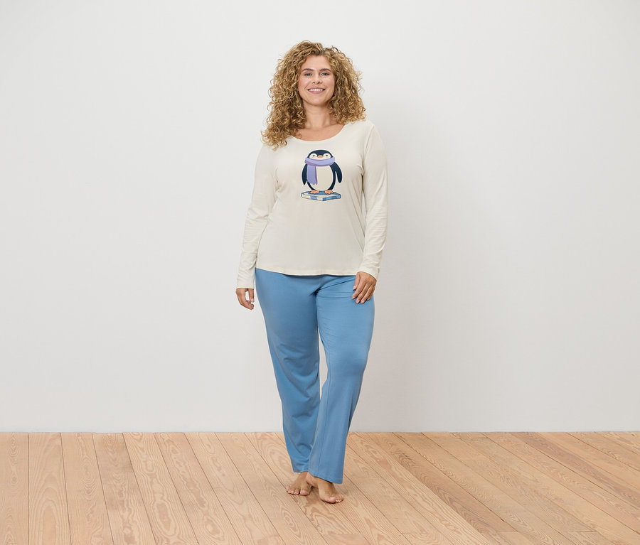 Frau posiert in einem cremefarbenen Pyjama-Oberteil mit Pinguin-Print und einer blauen Pyjamahose.