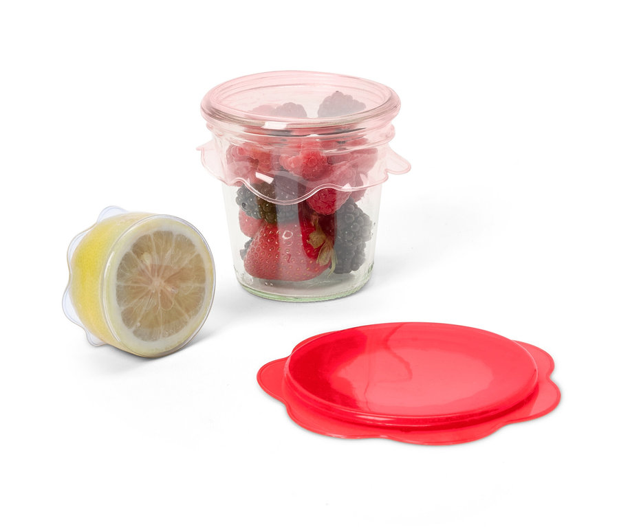Ein Glas mit Früchten ist mit einem 3 Silikon-Frischhaltedeckel abgedeckt, daneben eine Zitronenhälfte mit dem gleichen Deckel und ein roter Deckel.