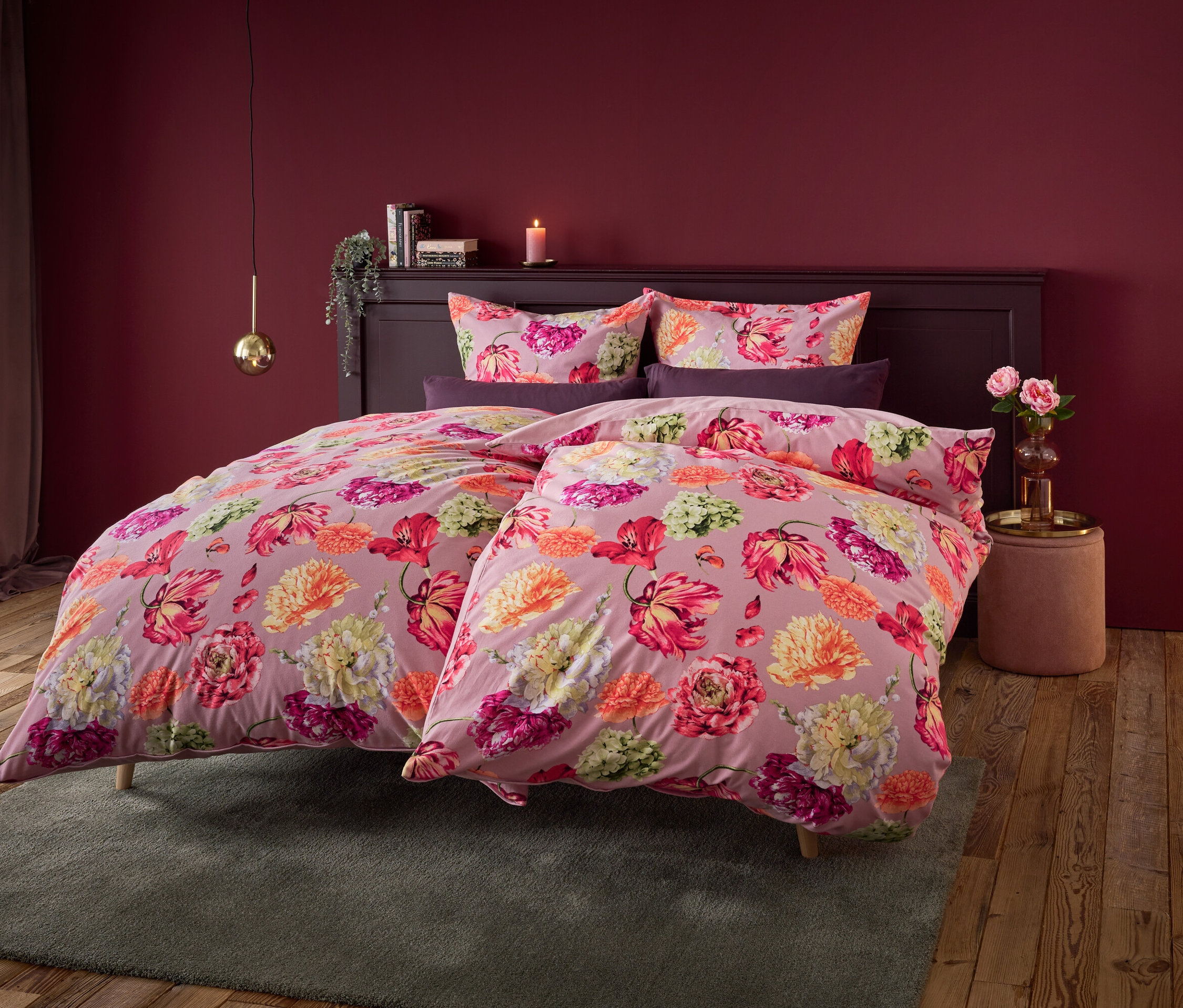 Blumenbettwäsche auf einem Bett mit einer dunkelroten Wand im Hintergrund.