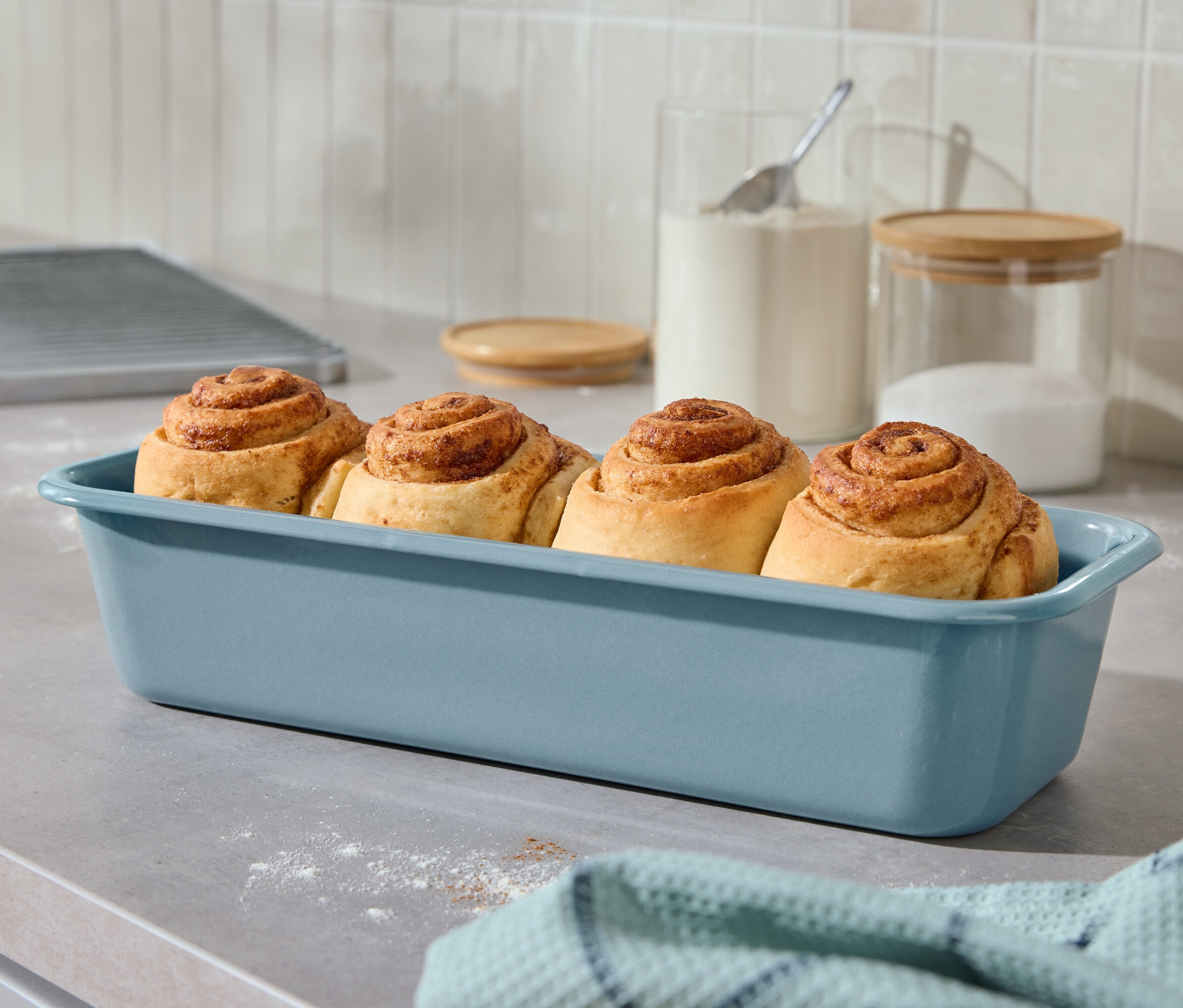 Vier Zimtschnecken in einer blauen Auflaufform auf einer Küchentheke.