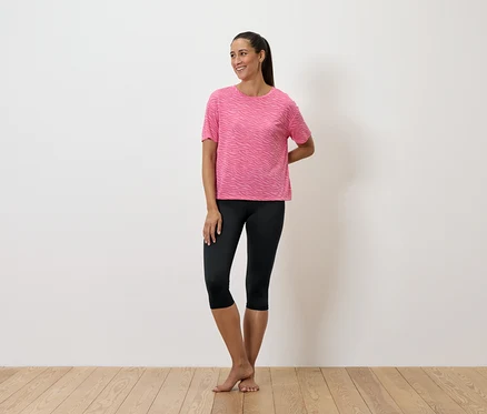 Eine Frau steht und trägt ein rosa T-Shirt und schwarze Leggings.