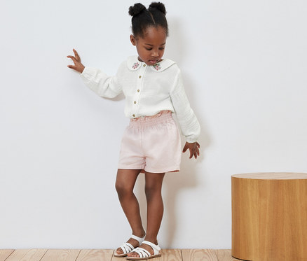 Mädchen tanzt in Kinder-Musselin-Bluse, rosa Shorts und Sandalen.