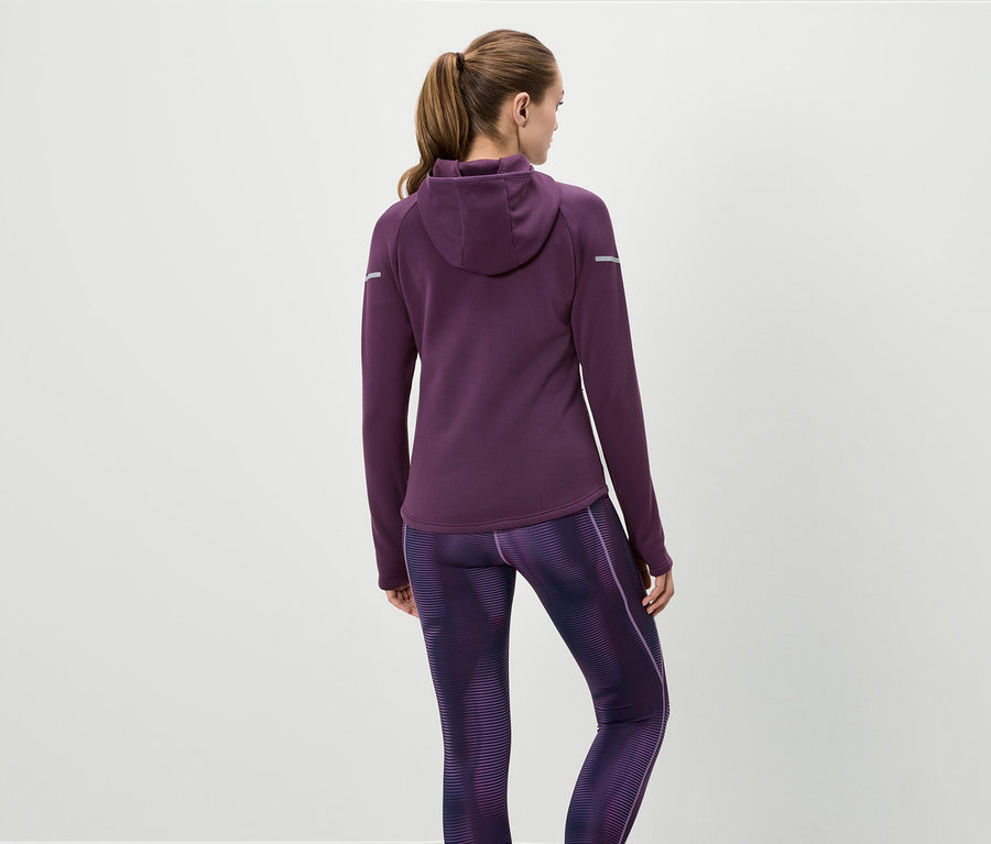 Eine Frau von hinten trägt einen lila Kapuzenpullover und gemusterte Leggings.