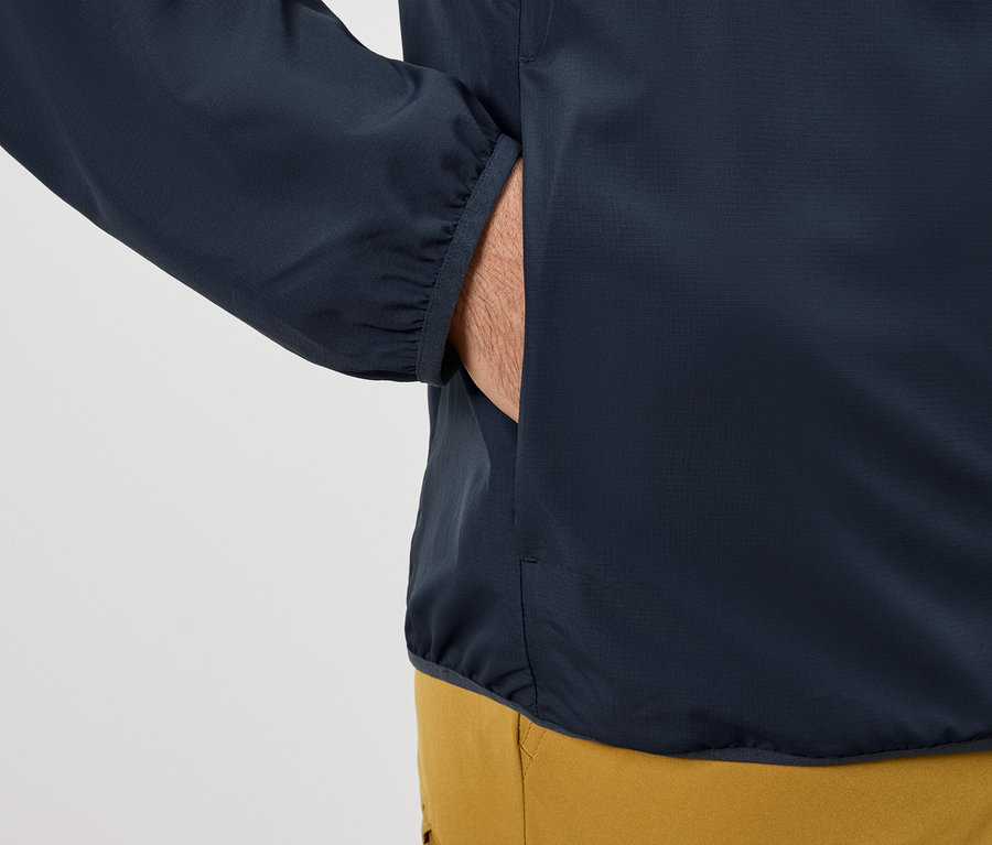 Mann steckt Hand in die Tasche einer dunkelblauen Jacke.