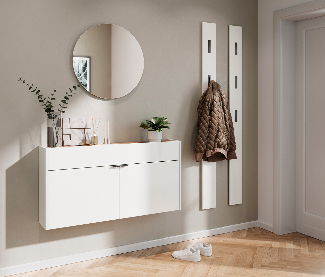 Eingangsbereich mit einem breiten, weißen Mehrzweckschrank »Ameca«, einem runden Spiegel und einer Jacke an einer weißen Garderobe.
