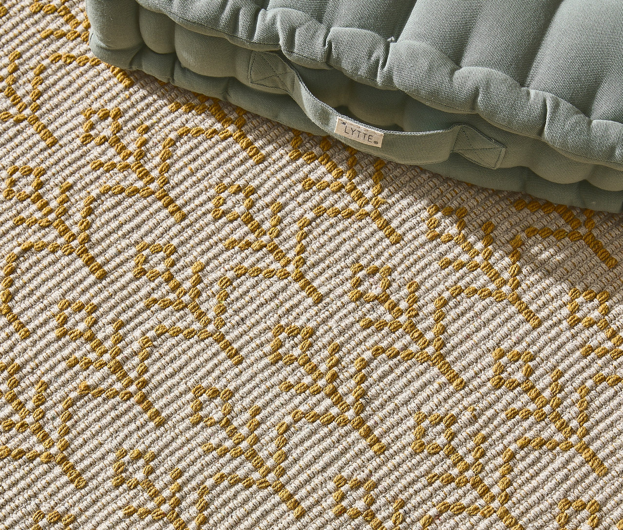 Nahaufnahme eines Teppichs mit gelbem geometrischem Muster und einem hellgrünen Sitzkissen.