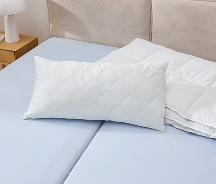 Ein weißes Kopfkissen Cell Solution®, 80 x 40 cm, liegt auf einem blauen Bett neben einer weißen Bettdecke.