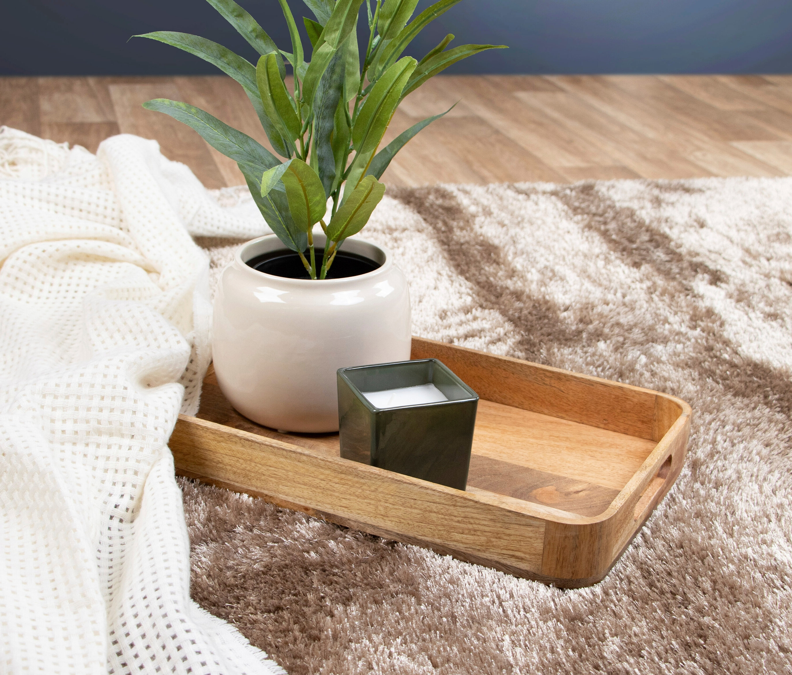Auf einem hellbraunen Teppich »Silky« liegen ein Tablett mit einer Topfpflanze und einer Kerze sowie eine weiße Decke.