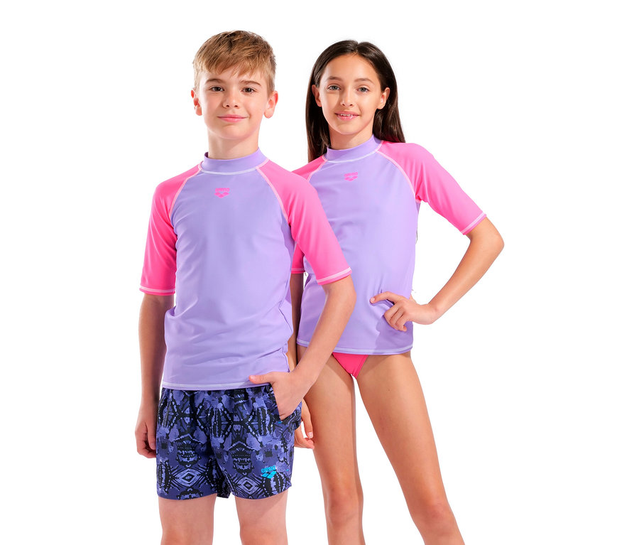 Ein Junge in Badehose und ein Mädchen in rosa Bikini und lila Rashguard-Shirts stehen nebeneinander.