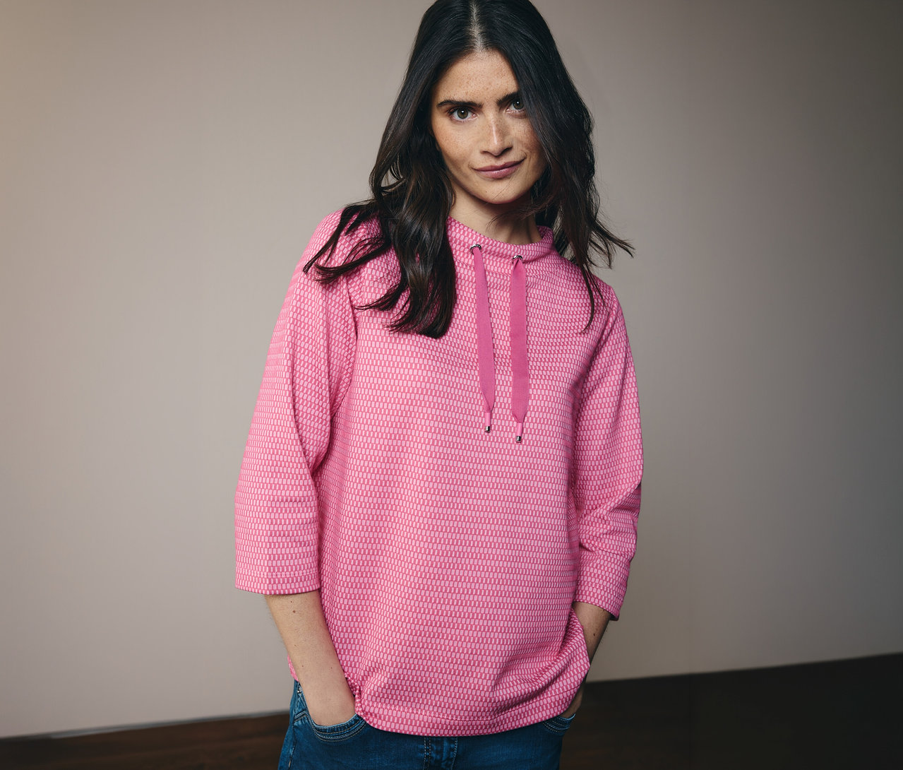 Frau mit Jeans und pinkem CECIL Sweatshirt mit Kapuze und Kordel. Sie hat die Hände in den Hosentaschen.