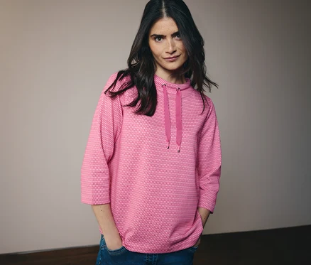Frau mit Jeans und pinkem CECIL Sweatshirt mit Kapuze und Kordel. Sie hat die Hände in den Hosentaschen.