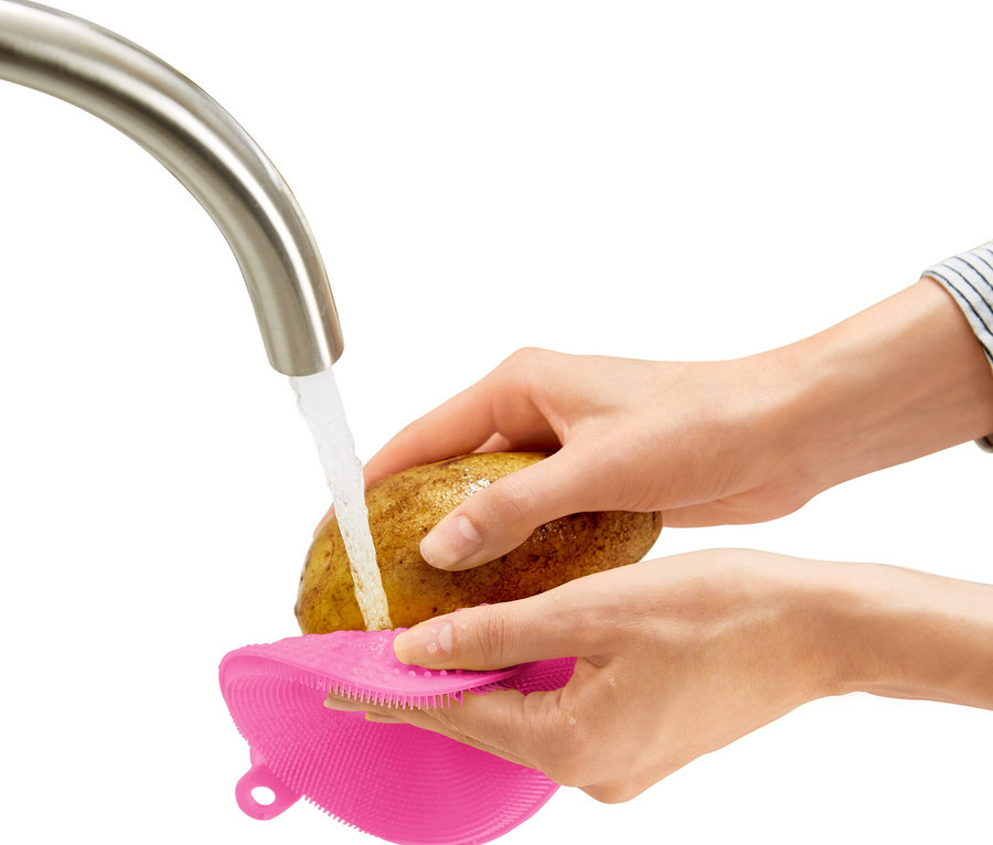 Eine Person wäscht eine Kartoffel mit einer pinken Bürste unter einem Wasserhahn.