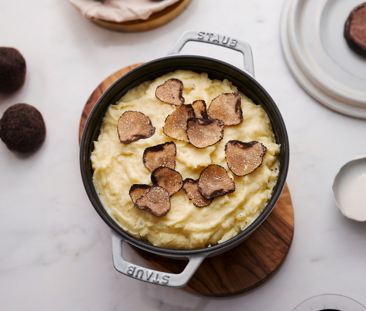 Draufsicht auf eine STAUB »Cocotte 24« in Weiß mit ca. 3,7 l, gefüllt mit Kartoffelpüree und Trüffelscheiben, auf einem Holzteller.