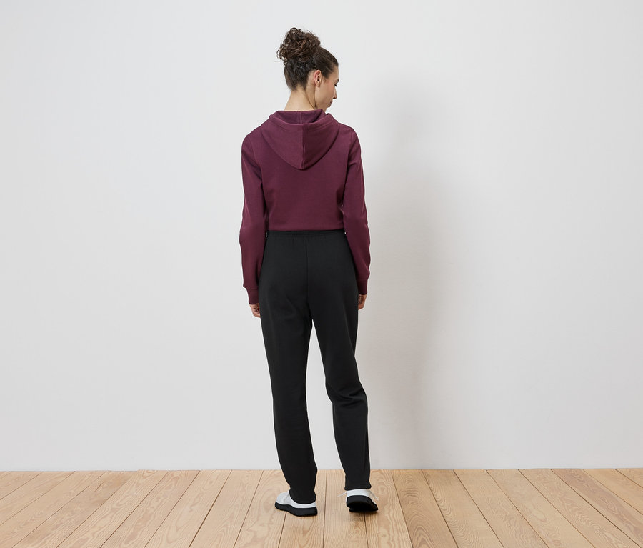 Frau von hinten, trägt einen bordeauxroten Kapuzenpullover und schwarze Hosen.