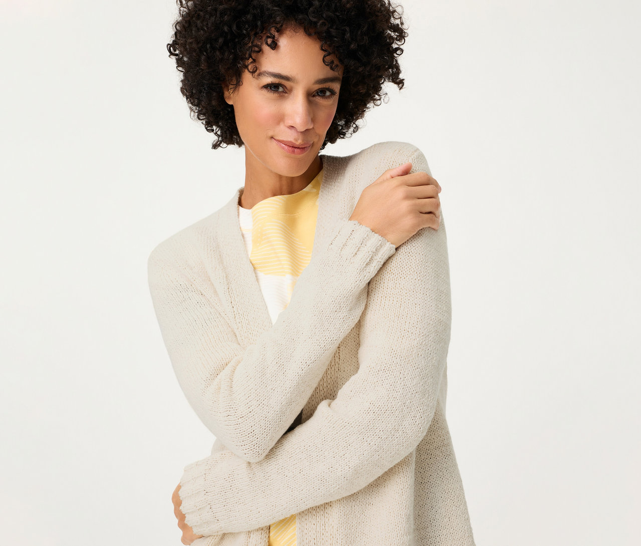 Frau mit lockigem Haar umarmt sich selbst und trägt einen Olsen Leinen-Cardigan über einem gelb gestreiften Oberteil.