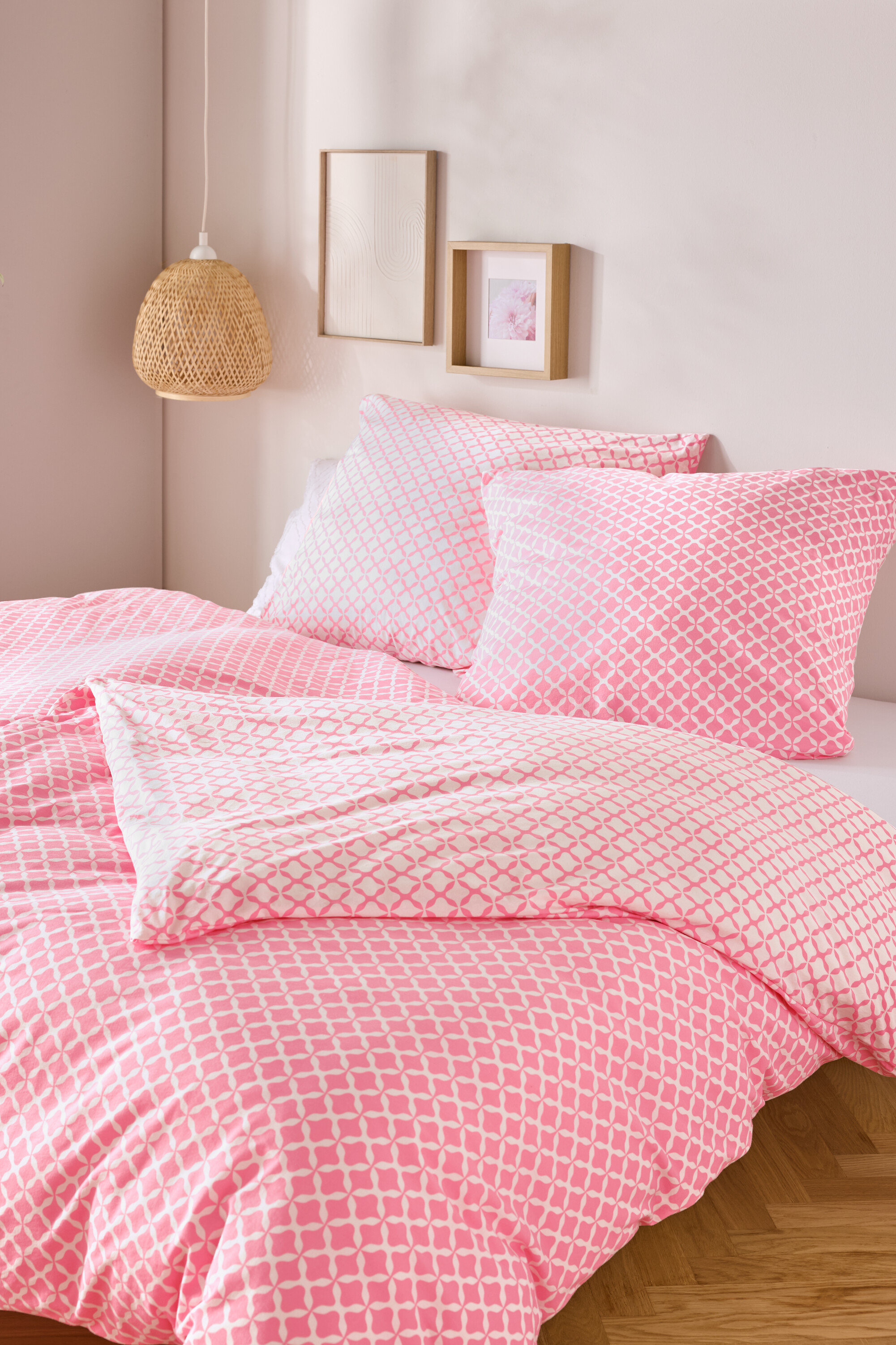 Nahaufnahme von einem Bett mit rosa-weisser Jersey-Bettwäsche, Normalgrösse und Übergrösse, mit zwei Kissen und einer Decke.