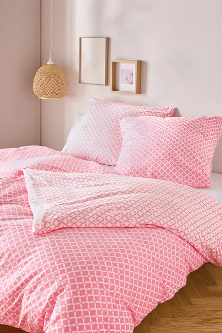 Nahaufnahme von einem Bett mit rosa-weisser Jersey-Bettwäsche, Normalgrösse und Übergrösse, mit zwei Kissen und einer Decke.
