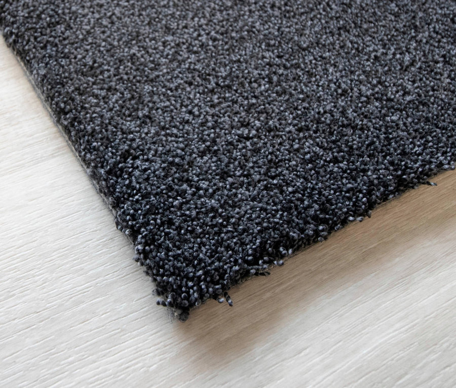 Nahaufnahme eines anthrazitfarbenen Teppichs »Jane« auf einem hellen Holzboden.
