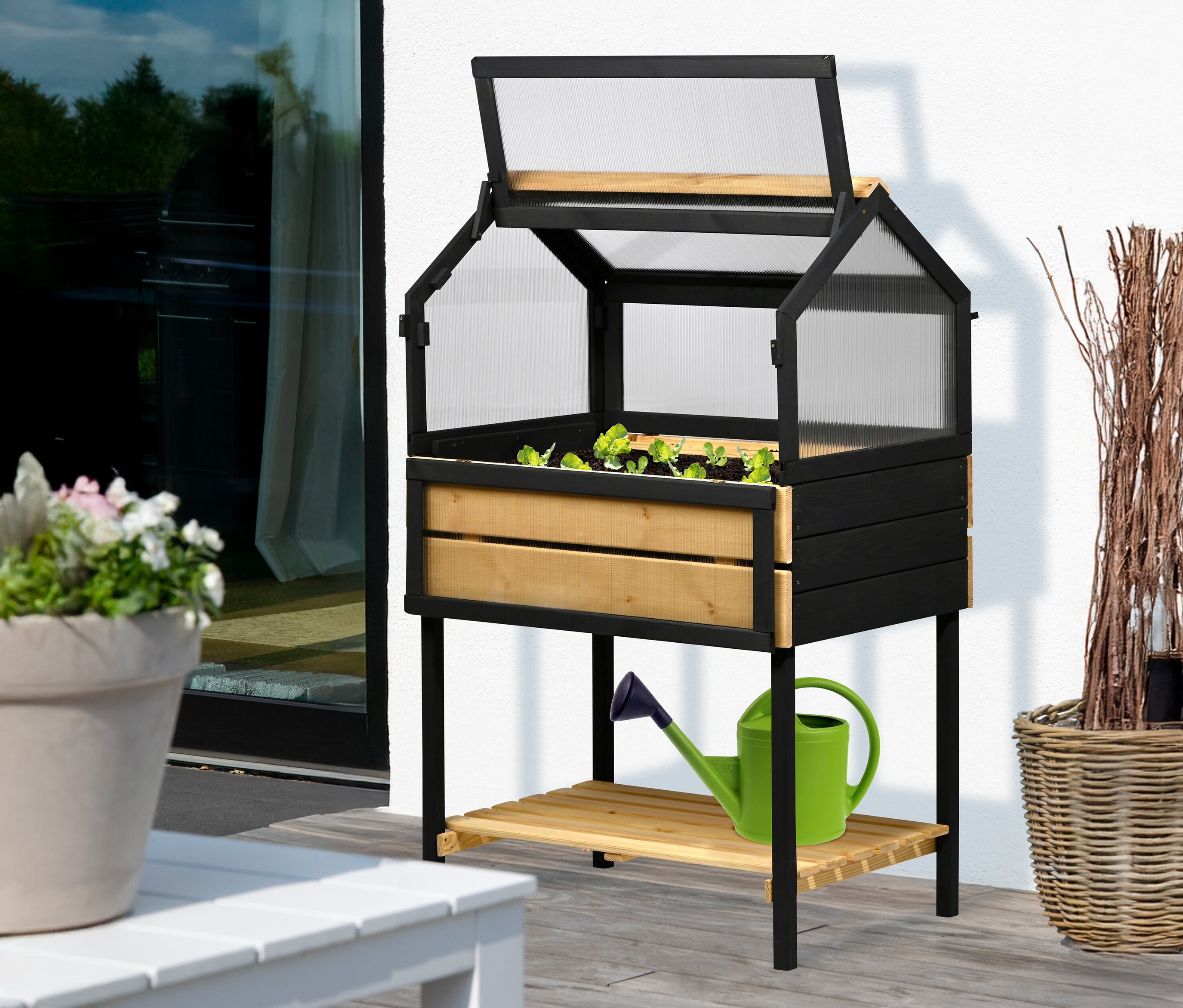 Ein 4-Jahreszeiten-Hochbeet, L mit Salatpflanzen steht auf einer Terrasse, daneben eine Gießkanne.