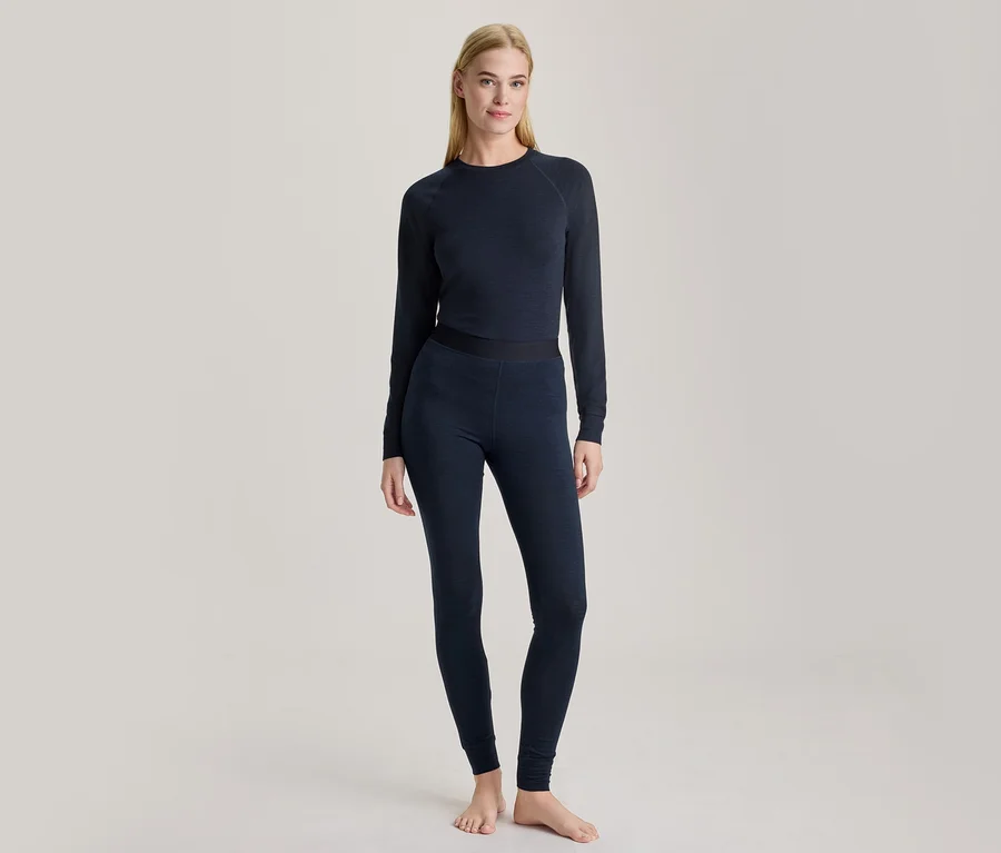 Eine blonde Frau steht barfuß und trägt ein dunkelblaues Langarmshirt und passende Leggings.
