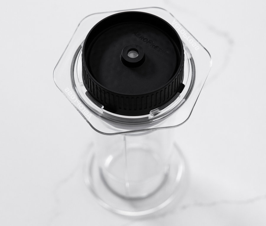 Ein transparenter AeroPress Coffee Maker »Clear« steht auf einer weißen Oberfläche.