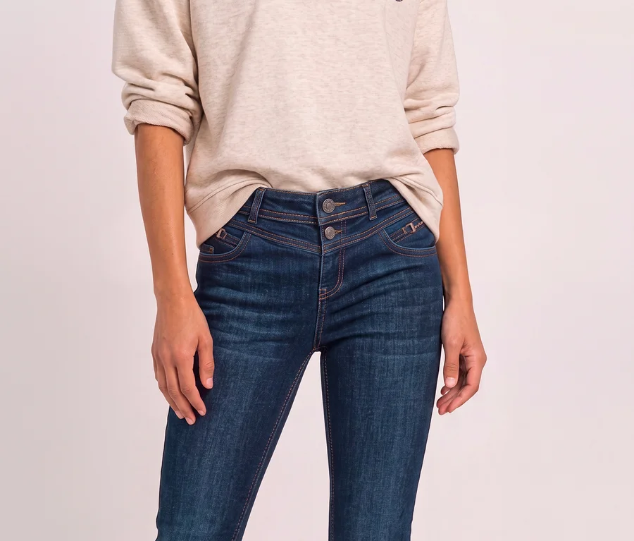 Eine Person trägt ein beiges Sweatshirt und blaue Street One Jeans mit doppelter Knopfleiste und sichtbaren Nähten.