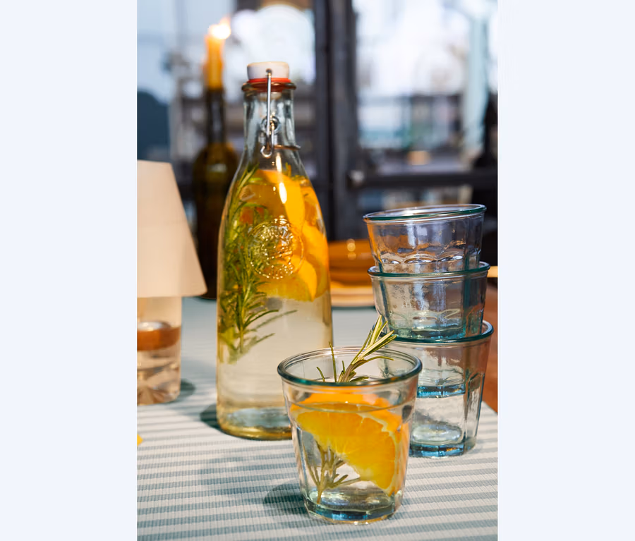 Glasflasche mit Bügelverschluss und 4 Trinkgläser auf einem Tischläufer.