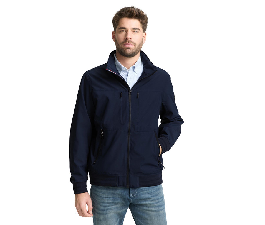 Mann mit Tom Tailor Blouson-Jacke in Sky Captain Blue und Jeans, eine Hand in der Tasche.