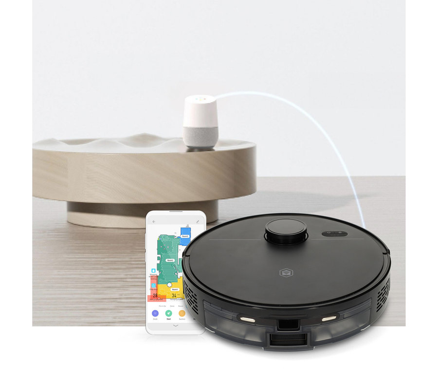 Ein schwarzer Saugroboter, ein weißes Smartphone mit einer bunten Reinigungsplan-Karte und ein weiß-grauer Smart Speaker auf einer hellen Holzoberfläche. Ein hellblauer Bogen verbindet den Smart Speaker mit dem Roboter.