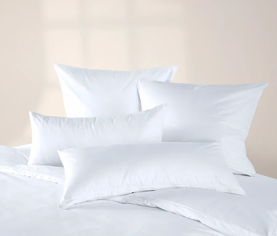 Vier offwhite Jersey-Kopfkissenbezüge auf einem Bett mit weisser Bettwäsche.