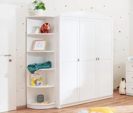 Ein weißes Pinolino Eckregal steht neben einem weißen Kleiderschrank und einer weißen Kommode in einem Kinderzimmer.