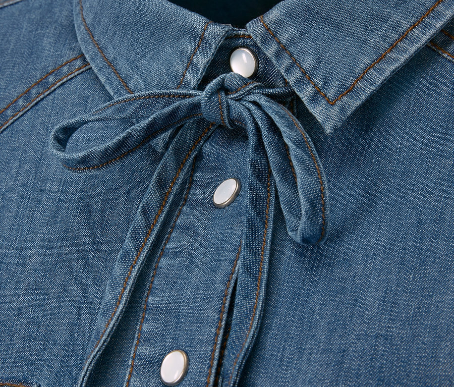 Detail einer Jeansbluse mit Knopfleiste und Bindeband.