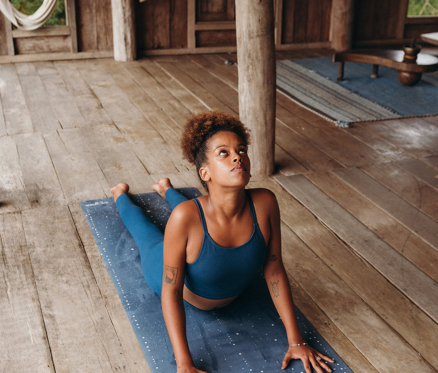 Junge Frau macht Yoga in einem blauen Set auf einer blauen Matte mit weißen Punkten.