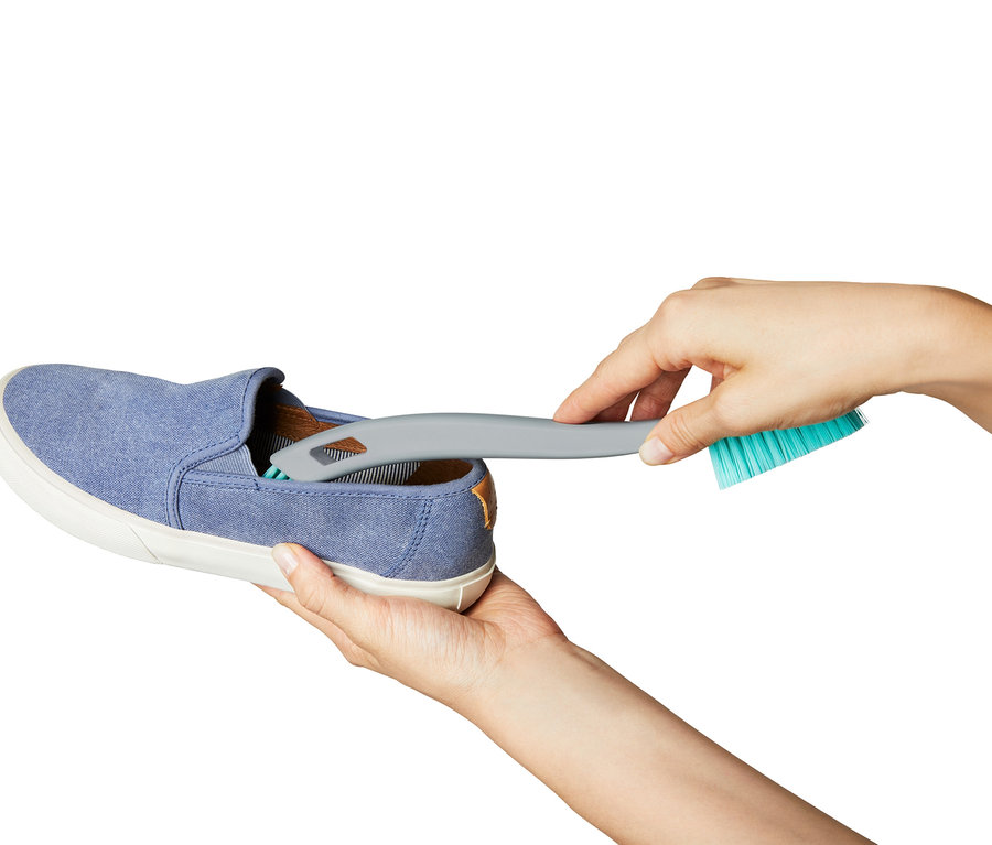 Hände reinigen einen blauen Stoffschuh mit einer 2-in-1-Schuhreinigungsbürste.