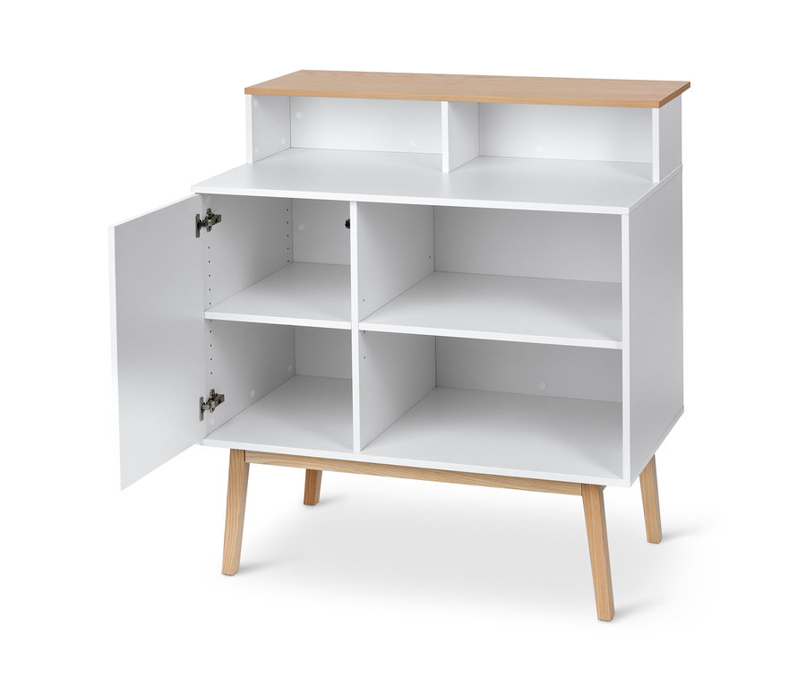 Ein weisser Bar mit Tresen steht vor hellem Hintergrund, eine Tür ist offen und gibt den Blick auf die inneren Regale frei.