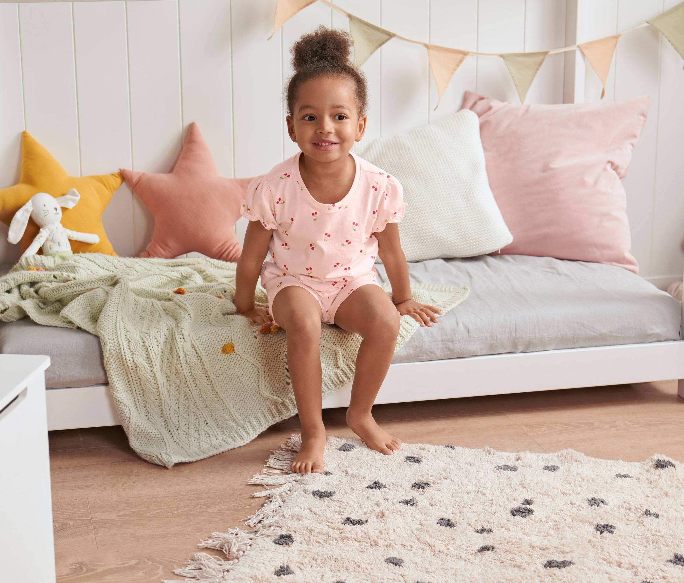 Ein Mädchen sitzt in einem Shorty-Pyjama auf einem Bett.