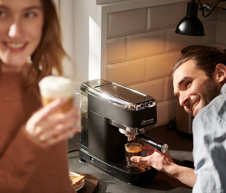 Mann bereitet Espresso mit »Lapressa« Siebträgermaschine, schwarz, zu, Frau hält Latte.