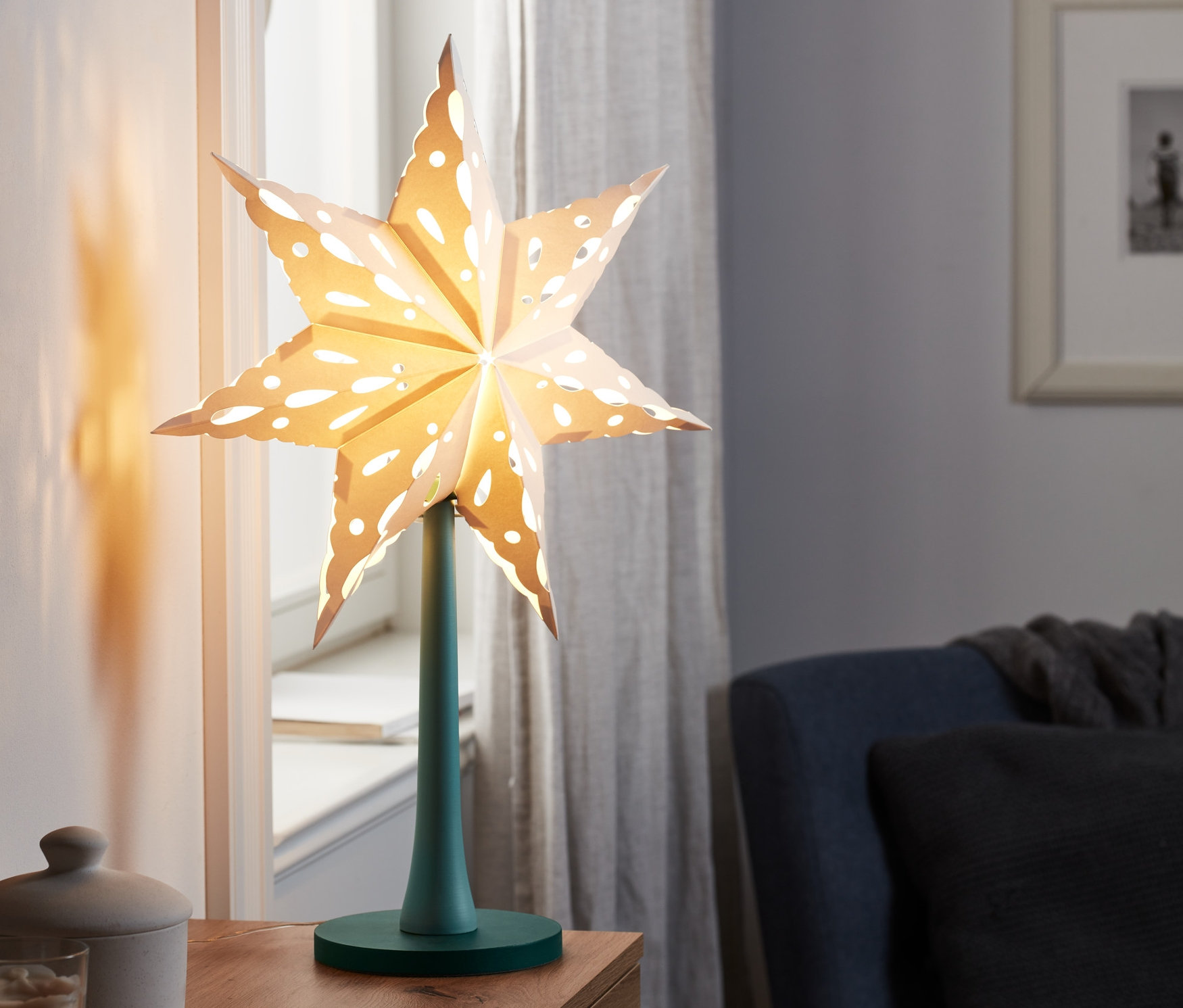 LED-Papierstern mit Holzfuß steht auf einem Holztisch.
