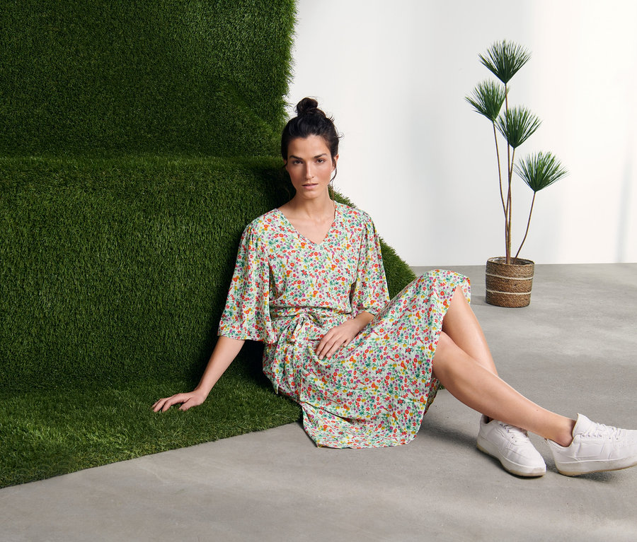 Eine Frau sitzt auf dem Boden neben einer grünen Wand und trägt ein Kleid mit Print.