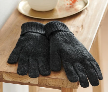 Ein Paar anthrazitfarbene Strickhandschuhe mit Wolle liegen auf einem Holzhocker.