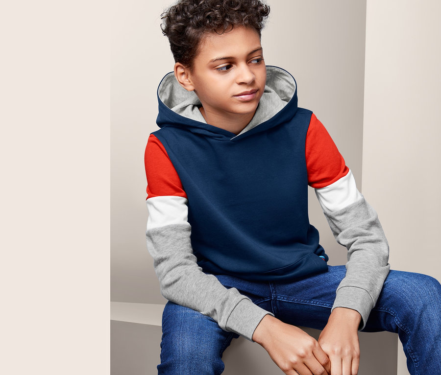 Ein Junge sitzt und trägt einen Hoodie.