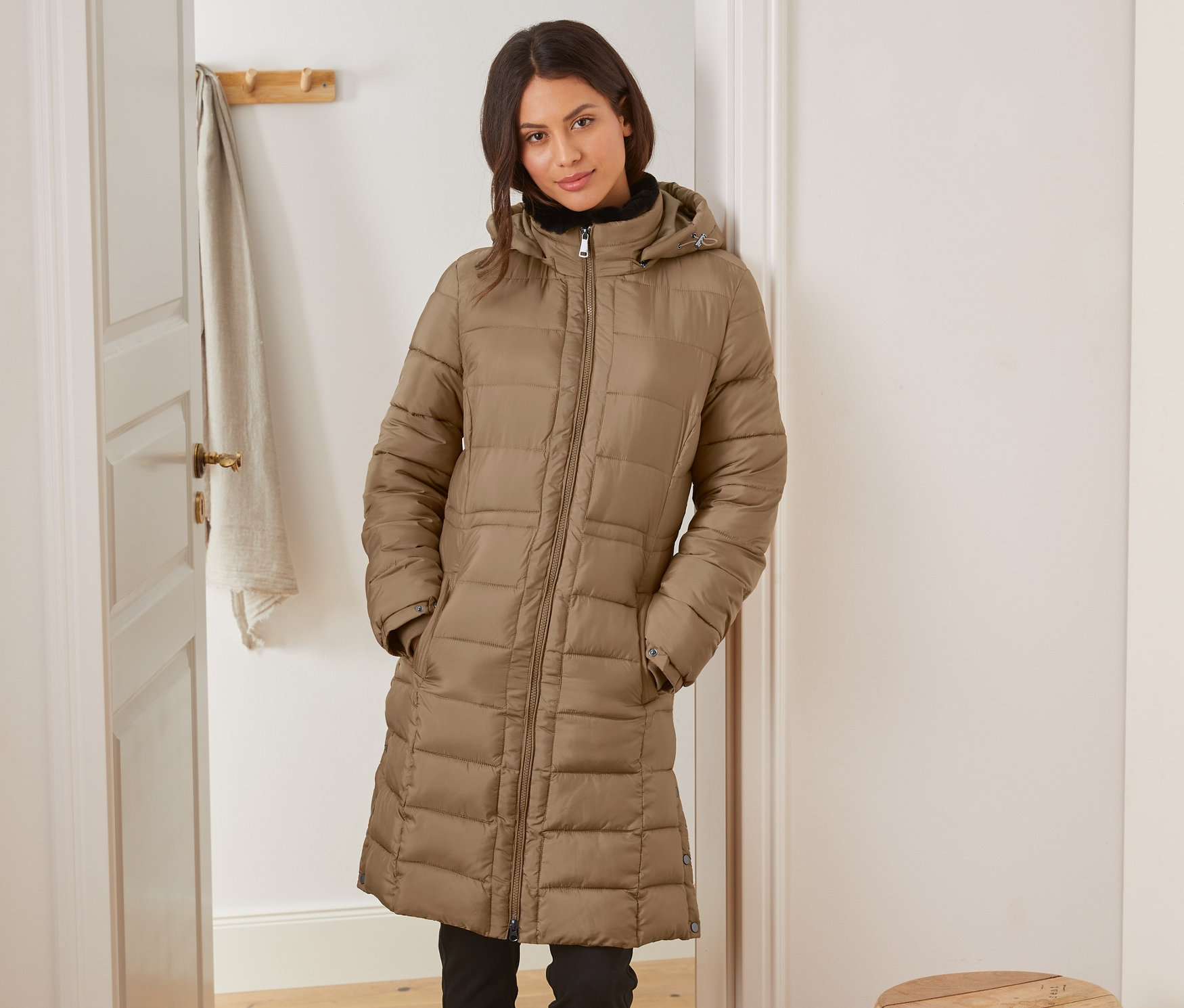 Frau posiert in einem Steppmantel mit Kapuze in einer Tür.