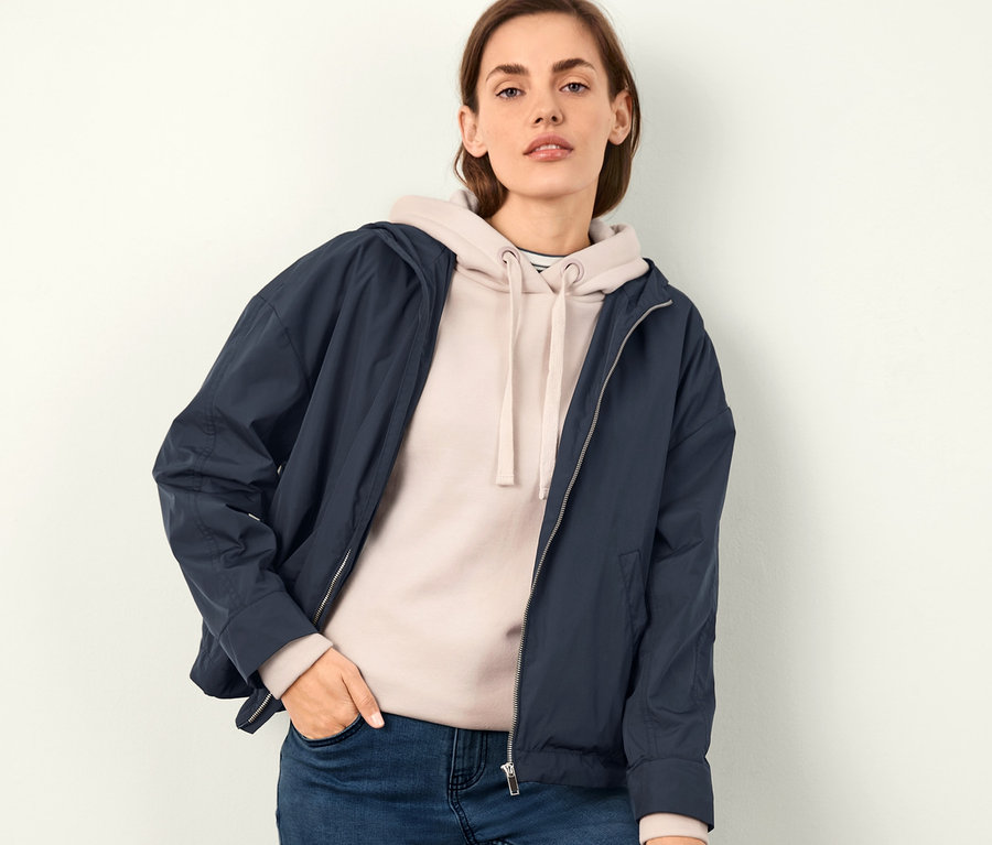 Frau posiert in kurzem Parka mit Kapuze, Hoodie und Jeans.