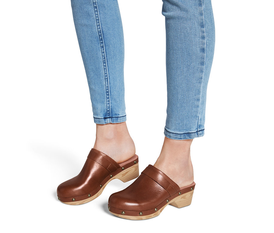 Beine in Jeans und Leder-Clogs.