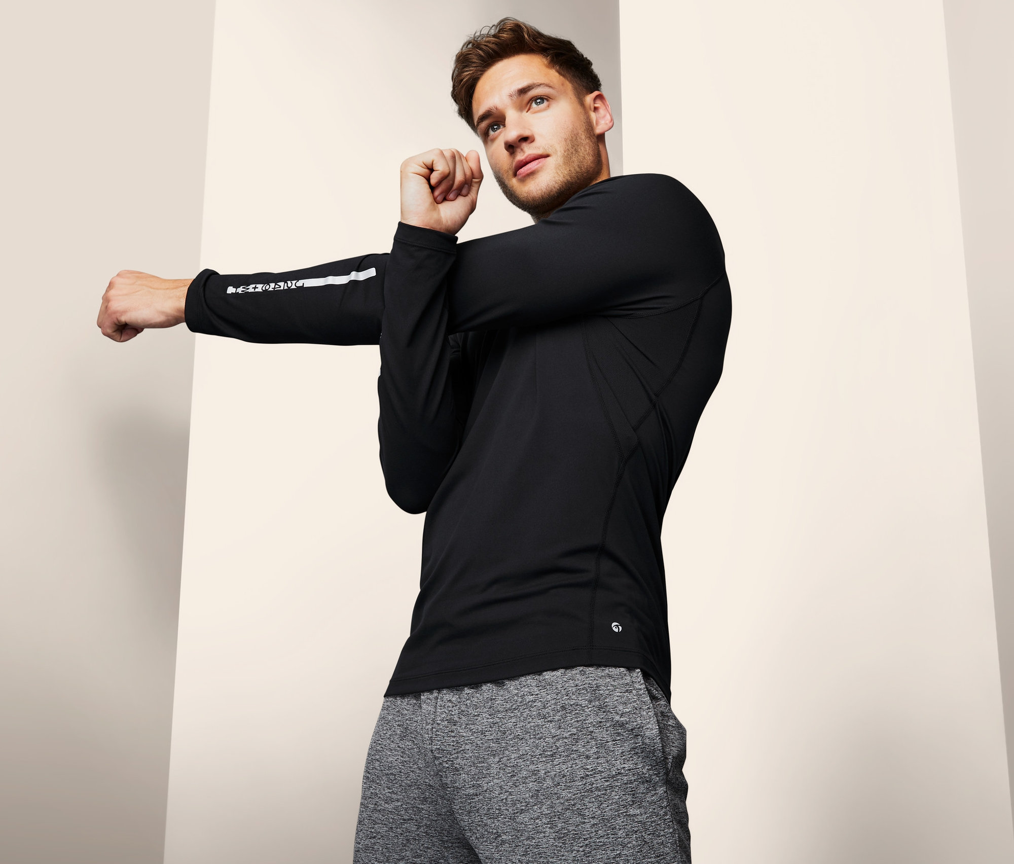 Mann dehnt Arm in schwarzem Langarm-Funktionsshirt.